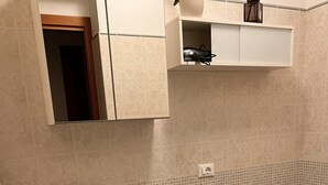 Un baño con lavabo, inodoro y espejo sobre el lavabo. Hay un mueble pequeño encima del lavabo y una repisa con una lámpara.