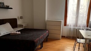 Un dormitorio con cama, mesita de noche, lámpara y un escritorio con silla.
