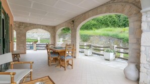 A covered patio with a table and chairs, stone arches, and potted plants.