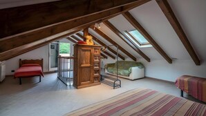 A loft bedroom with a sloped ceiling, a wooden cabinet, a bed, a sofa, and a window providing natural light.