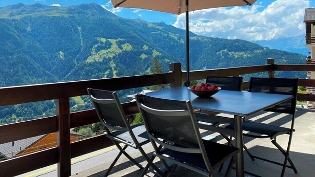 A terrace with a table and chairs, a bowl of fruit, and a large umbrella.