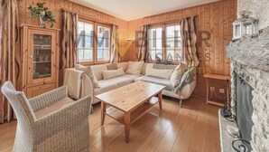 A cozy living room with wooden walls, a sofa, a wicker chair, and a wooden table.