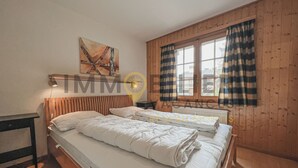 A room with two beds, wooden walls, a window with curtains, and a painting on the wall.