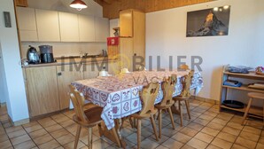 A dining area with a table set for four, wooden chairs, a kitchen in the background, and a framed picture on the wall. - Located at the entrance to the village, right next to the shuttle bus stop and the supermarket, this (St-Luc)