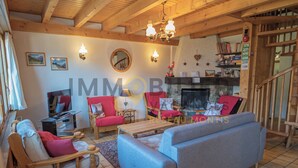 A cozy living room with a fireplace, wooden beams, a bookshelf, and comfortable seating. - Located at the entrance to the village, right next to the shuttle bus stop and the supermarket, this (St-Luc)