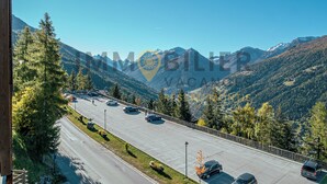 A parking lot with cars, surrounded by mountains and trees. - Located at the entrance to the village, right next to the shuttle bus stop and the supermarket, this (St-Luc)