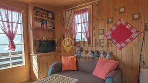 A cozy cabin interior with a sofa, a small table, wooden shelves, a television, and a window with curtains. - A charming chalet with a parking space, rustic yet practical, spread over two floors, with a magnifi (St-Luc)
