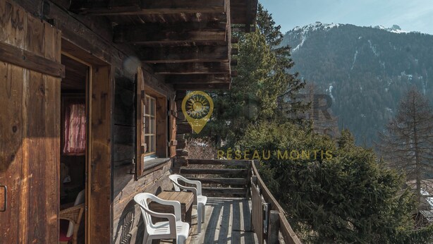 A wooden cabin with a balcony, white plastic chairs, and a mountain backdrop. - A charming chalet with a parking space, rustic yet practical, spread over two floors, with a magnifi (St-Luc)