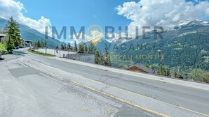 Une route avec une chaîne de montagnes en arrière-plan, un panneau indiquant le « Chalet de Sainte-Lucie », et une vue sur des montagnes enneigées.