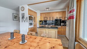 Un coin repas avec une table et des chaises en bois, une cuisine avec des meubles et des appareils électroménagers en bois, et une fenêtre avec des rideaux.