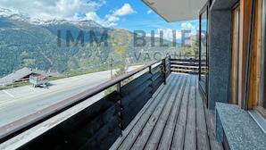 A balcony with a view of a mountain landscape, a parking area, and a building with large windows.