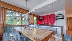 A modern kitchen with a wooden table and chairs, a red accent wall, and a large window.