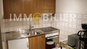 A kitchen with wooden cabinets, a stainless steel sink, a microwave, and a coffee maker. - Situé à l'entrée du village, à proximité immédiate du bus navette et des commerces. Idéal pour 2 à 4 (St-Luc)