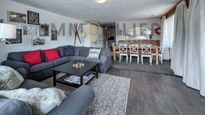 A modern living room with a grey sofa, red cushions, a black coffee table, and a dining area with white chairs and a wooden table.