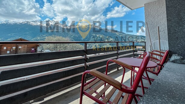 A balcony with a view of snow-capped mountains, wooden steps, and red chairs.