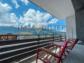 A balcony with a view of snow-capped mountains, wooden steps, and red chairs. - Located at the entrance of the village, close to the shuttle bus and shops. Ideal for 7 to 8 people, (St-Luc)
