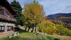 Ein rustikales Steinhaus mit Holzbalkon, umgeben von Herbstlaub und einer Bergkulisse.