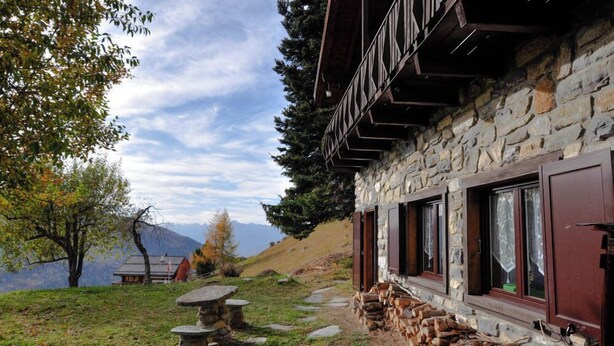 Ein Steinhaus mit Holzbalkon, einem Steintisch und einem Holzstapel.