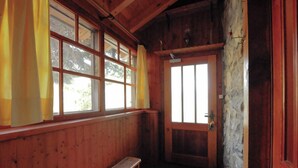 Ein Zimmer mit Holzboden, einer Bank, großen Fenstern mit Vorhängen und einer Steinwand.