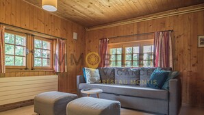 A cozy room with wooden walls, a grey sofa with cushions, two grey ottomans, and a small round table. - Chalet en bois de mélèze, typique et authentique avec énormément de charme. Idéal pour les familles, (St-Luc)
