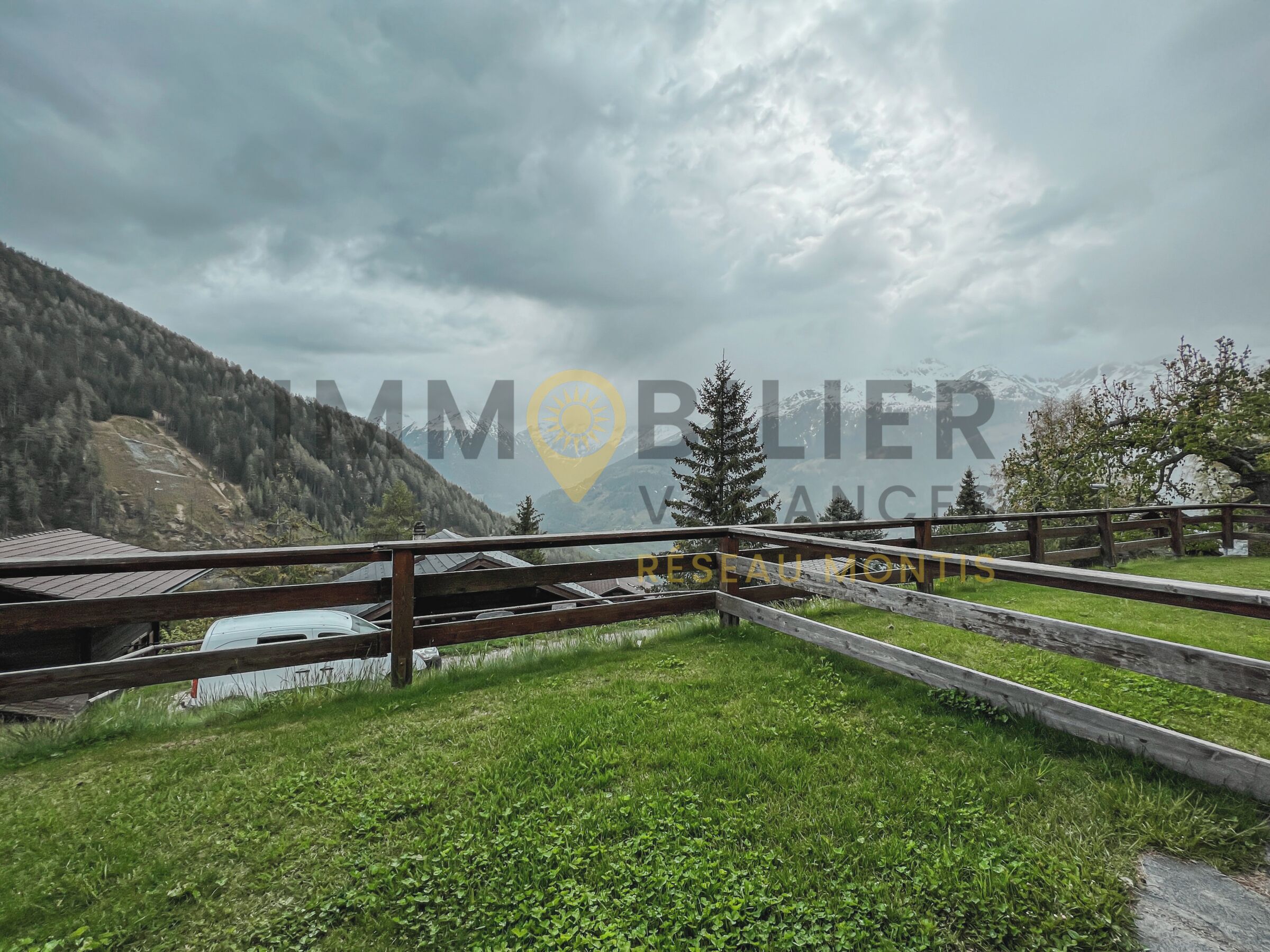A mountainous landscape with a wooden fence and a small building.