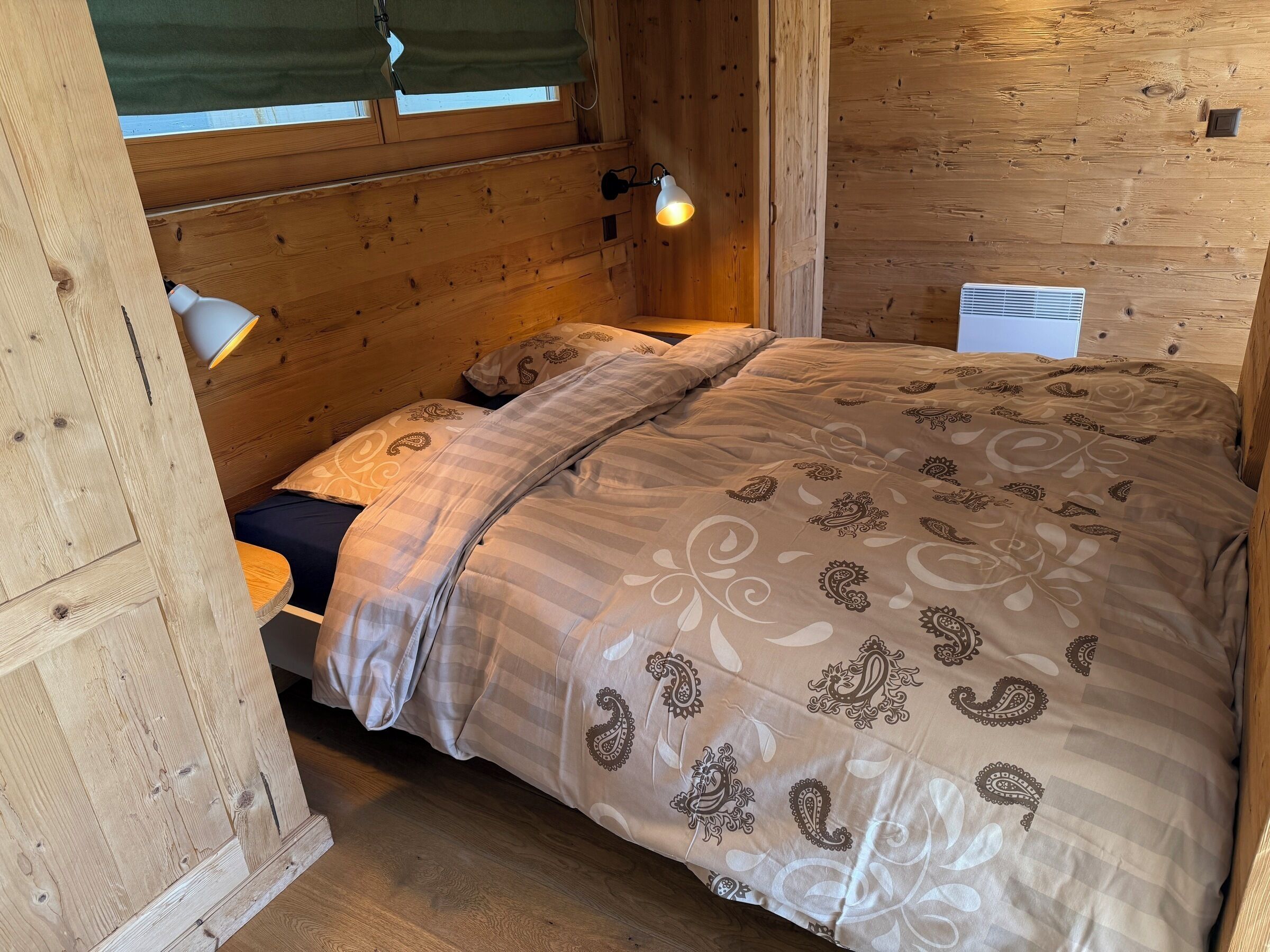 A wooden cabin-style room with a bed, a nightstand, a lamp, and a window.