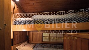 A bunk bed room with a wooden ceiling and walls, a small wooden nightstand, and a window with a view of the outside. - Ce charmant chalet est parfait pour accueillir une famille de 4 personnes. Vous trouverez deux chamb (Chandolin)