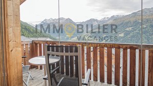 Une terrasse en bois avec une table et des chaises, offrant une vue sur un paysage montagneux.