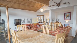 Un salon chaleureux avec une table à manger en bois, un ensemble de canapés et un téléviseur.