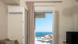 Un saló modern amb un sofà, una televisió i vista a l'oceà a través d'una porta oberta.