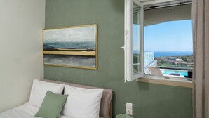 Un dormitori amb llit, almoines, un quadre, una finestra i vista al mar i a edificis.
