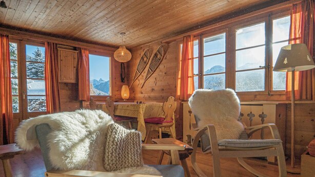 Interior acogedor de una cabaña con paredes de madera, ventanas amplias y una mecedora.