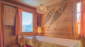 Una cabaña de madera con una mesa de comedor, sillas, una ventana que ofrece vistas a las montañas y un tapiz tejido en la pared.
