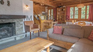 A cozy cabin interior with a stone fireplace, wooden furniture, and a view of the forest through large windows.
