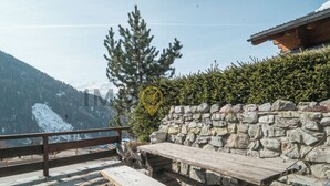 A wooden bench and picnic table set against a stone wall with a view of snow-capped mountains.