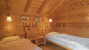 A wooden cabin room with two beds, a nightstand, and wall-mounted lamps.