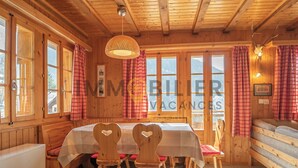A wooden cabin with a dining area, a bed, and a large window with curtains.
