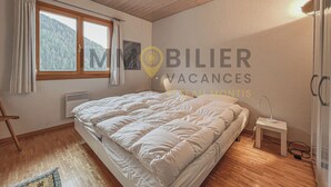 Een slaapkamer met een groot bed, een raam met gordijnen, een radiator, een klein nachtkastje met een lamp en een wandlamp.