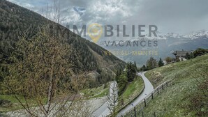 Berglandschap met een kronkelende weg, een klein gebouw en een bord met Mobilier Vacances Réseau Montis erop.
