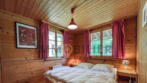 A wooden cabin bedroom with a bed, two windows with curtains, a ceiling light, and a framed picture on the wall. - Charming detached two-storey chalet for 7 (to 8) people. Splendid view of the Imperial Crown with th (St-Luc)