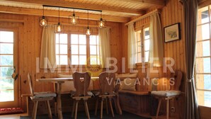 Una cabaña de madera con mesa y sillas, ventanas amplias y lámparas colgantes.