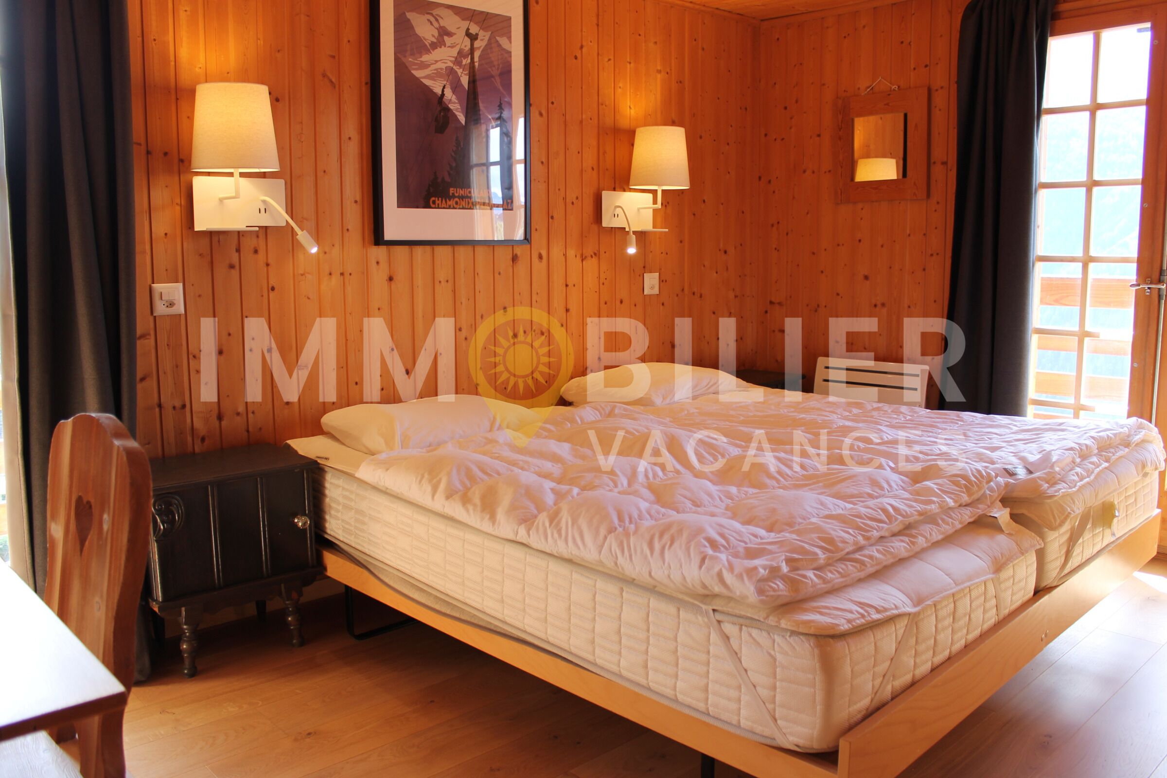 A wooden-paneled room with a bed, two wall-mounted lamps, a poster, and a small table.