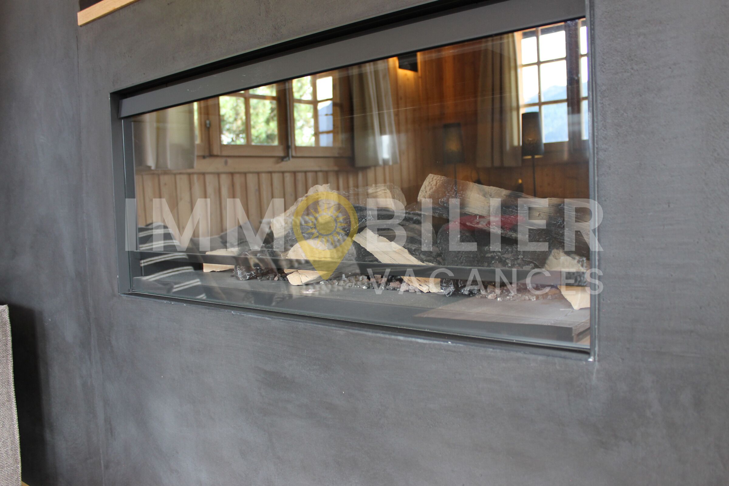 A window with a view of a room interior, including a bed and a window with a view of trees and mountains.