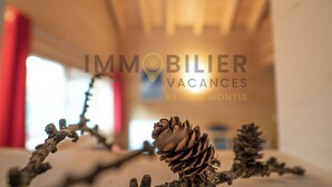 A blurred interior with a pine cone and a branch, and the text "IMMOBILIER VACANCES RÉSEAUX MONTIS". - Magnifique chalet confortable, moderne, de 195m2, 5 pièces  avec 4 chambres et pouvant accueillir ju (St-Luc)