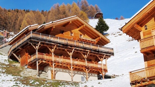 A wooden chalet with a balcony, set against a snowy mountain backdrop. - Magnifique chalet confortable, moderne, de 195m2, 5 pièces  avec 4 chambres et pouvant accueillir ju (St-Luc)