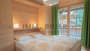 A wooden cabin room with a bed, a window with curtains, and a view of a wooden house outside. - Magnifique chalet confortable, moderne, de 195m2, 5 pièces  avec 4 chambres et pouvant accueillir ju (St-Luc)