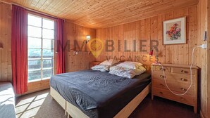 A wooden-paneled bedroom with a bed, a nightstand, a lamp, and a window with curtains.