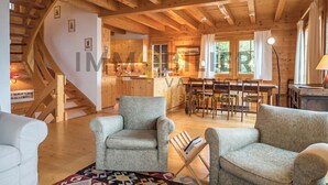 Un interior de madera con una escalera, dos sillones, una mesa de comedor y una zona de cocina.