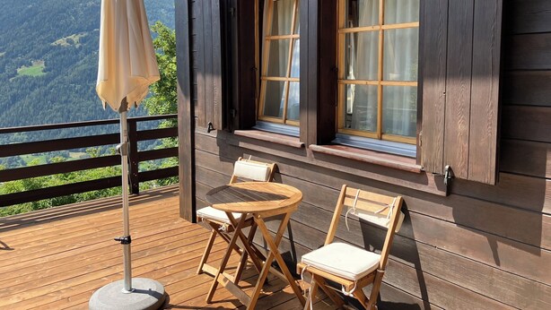 Una terraza de madera con una mesa y sillas, con vista a un paisaje montañoso.