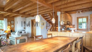 Amplia sala de estar con una mesa de comedor de madera, sillas y una zona de cocina con armarios de madera y una ventana.